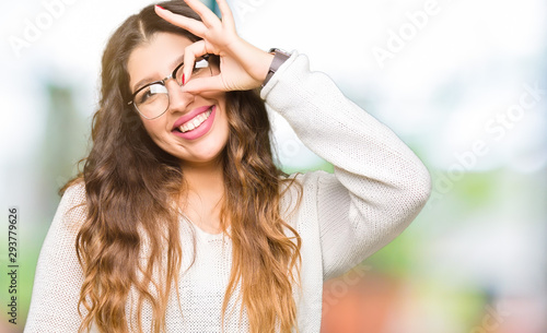Young beautiful woman wearing glasses doing ok gesture with hand smiling, eye looking through fingers with happy face.