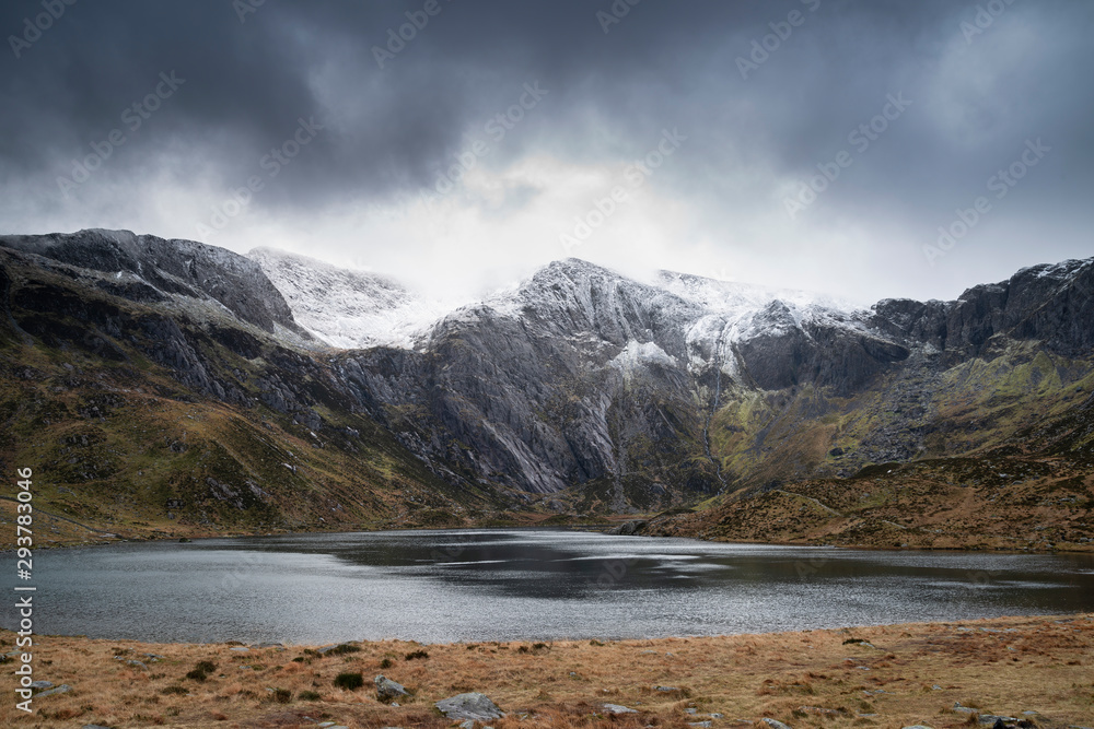 Beautiful moody Winter landscape image of Llyn Idwal and snowcapped Glyders Mountain Range in Snowdonia