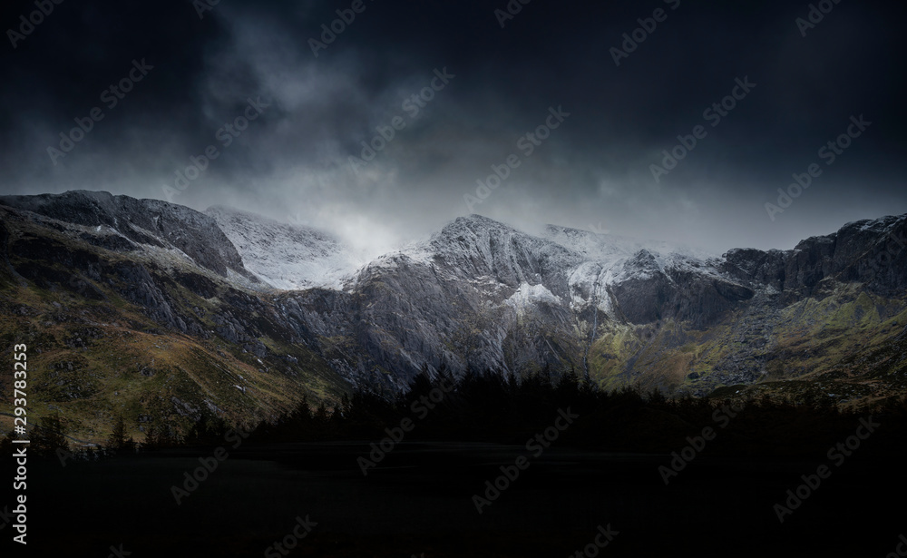 Beautiful moody Winter landscape image of Llyn Idwal and snowcapped Glyders Mountain Range in Snowdonia