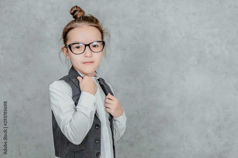 Little girl on a gray background. Dressed up as a business woman with black glasses. Isolated on a white background. Gesture class. Little girl on a gray background. Dressed up as a business woman with black glasses. Isolated on a white background. Gesture class.