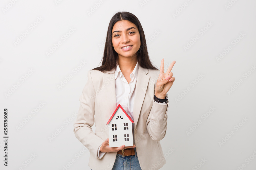 Young arab woman holding a house icon showing number two with fingers. Young arab woman holding a house icon showing number two with fingers.