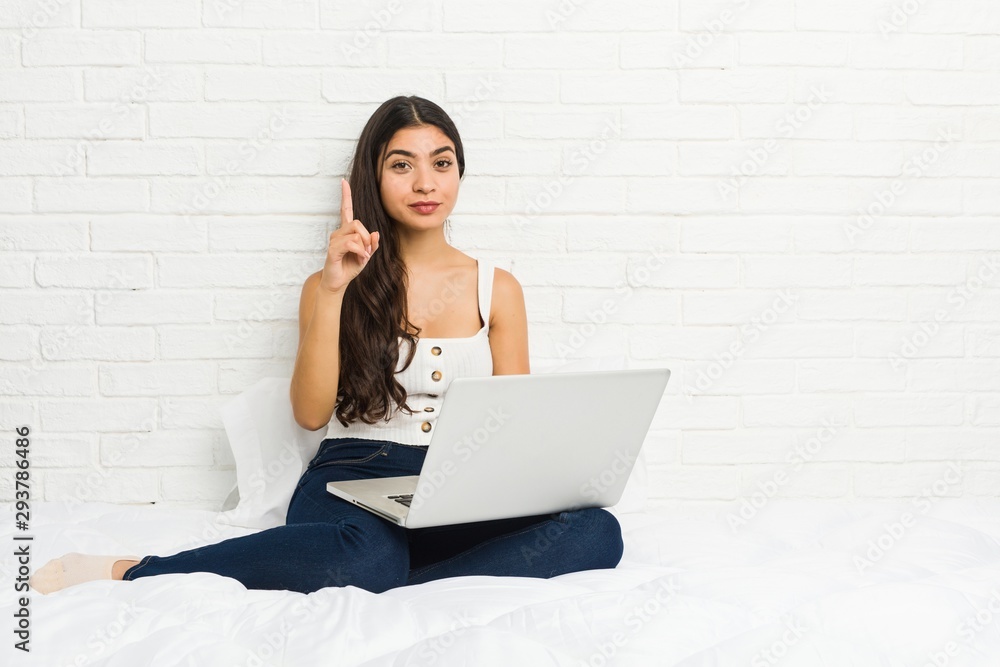 Young arab woman working with her laptop on the bed showing number one with finger. Young arab woman working with her laptop on the bed showing number one with finger.