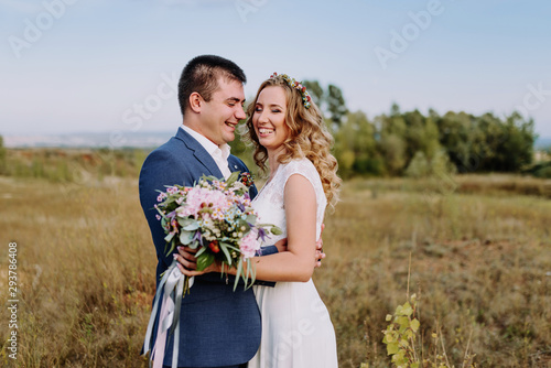 Wedding couple smiling. Beautiful bride and groom. Groom's boutonniere and bride’s wedding bouquet in hands.