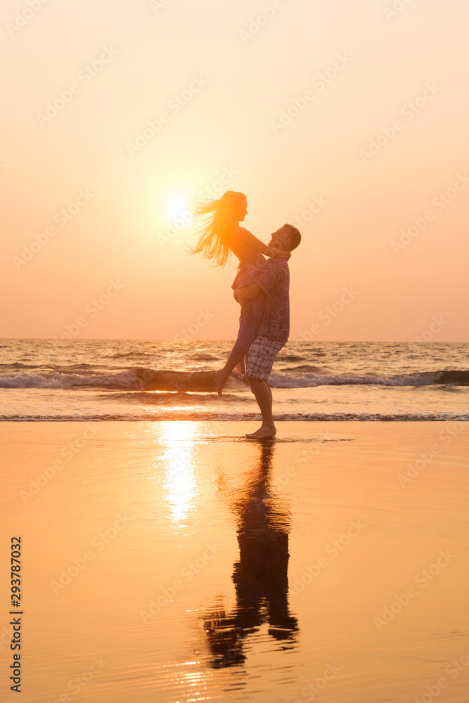 Romantic happy couple in love hugging and spinning at sunset beach, silhouettes of young man and woman on holidays or honeymoon 