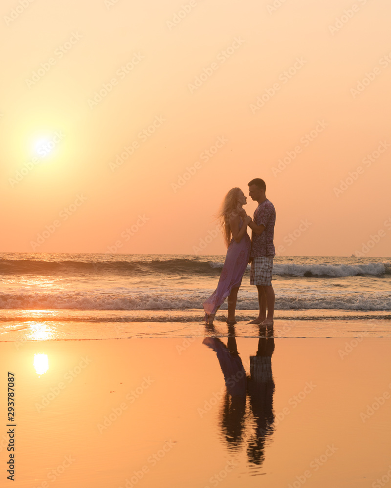 Silhouettes of young couple in love having a great time on the honeymoon staying on the beach with beautiful red sunset on background
