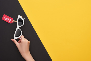 cropped view of woman holding glasses with sale label on yellow and black background