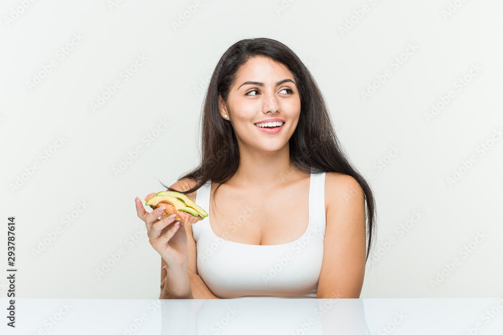 Young hispanic woman holding an avocado toast smiling confident with crossed arms. Young hispanic woman holding an avocado toast smiling confident with crossed arms.