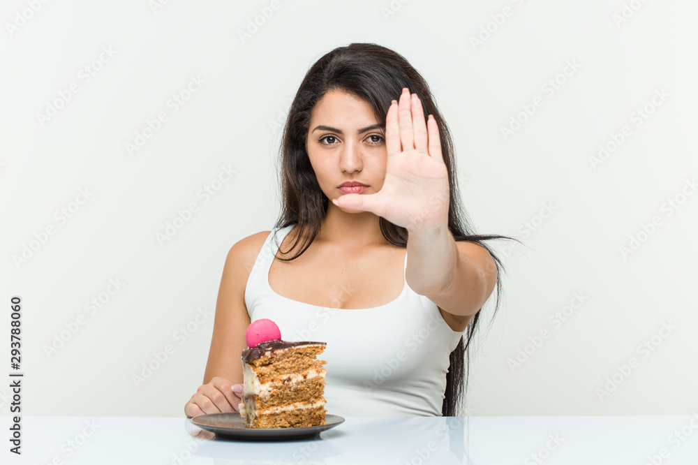 Young hispanic woman eating a cake standing with outstretched hand showing stop sign, preventing you. Young hispanic woman eating a cake standing with outstretched hand showing stop sign, preventing you.