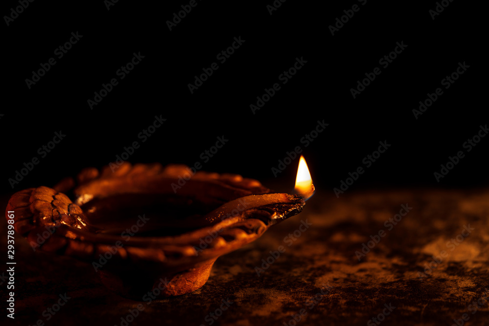 Burning Diwali Diya Clay Lamp. Diwali celebration background. Religious traditional illuminated diya oil clay lamp during Indian festive season isolated in black background with copy space.