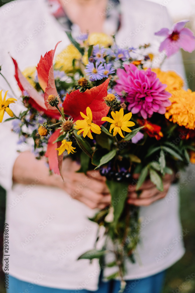 Grandmother with flowers in her hands. Hands of an old woman. Bouquet of flowers in the fall.