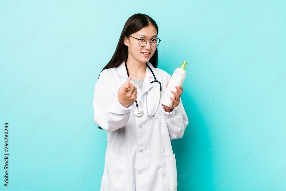 Young asian dermatologist girl pointing with finger at you as if inviting come closer. Young asian dermatologist girl pointing with finger at you as if inviting come closer.