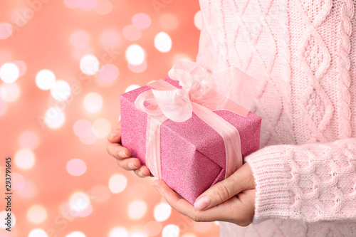 Woman holding beautiful Christmas gift on pink background, closeup. Bokeh effect