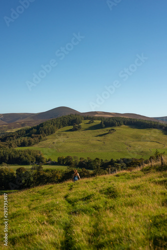 Young Woman Walking Through Fields Over the Crest of a Hill in Beautiful Natural Scenery in Scotland