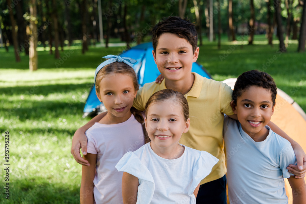 happy multicultural kids smiling near camps in park happy multicultural kids smiling near camps in park