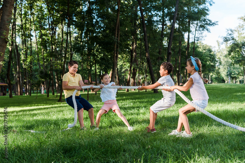 cheerful multicultural kids competing in tug of war outside