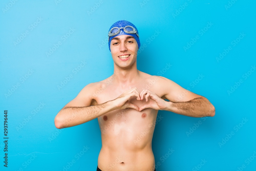 Young swimmer man smiling and showing a heart shape with hands.