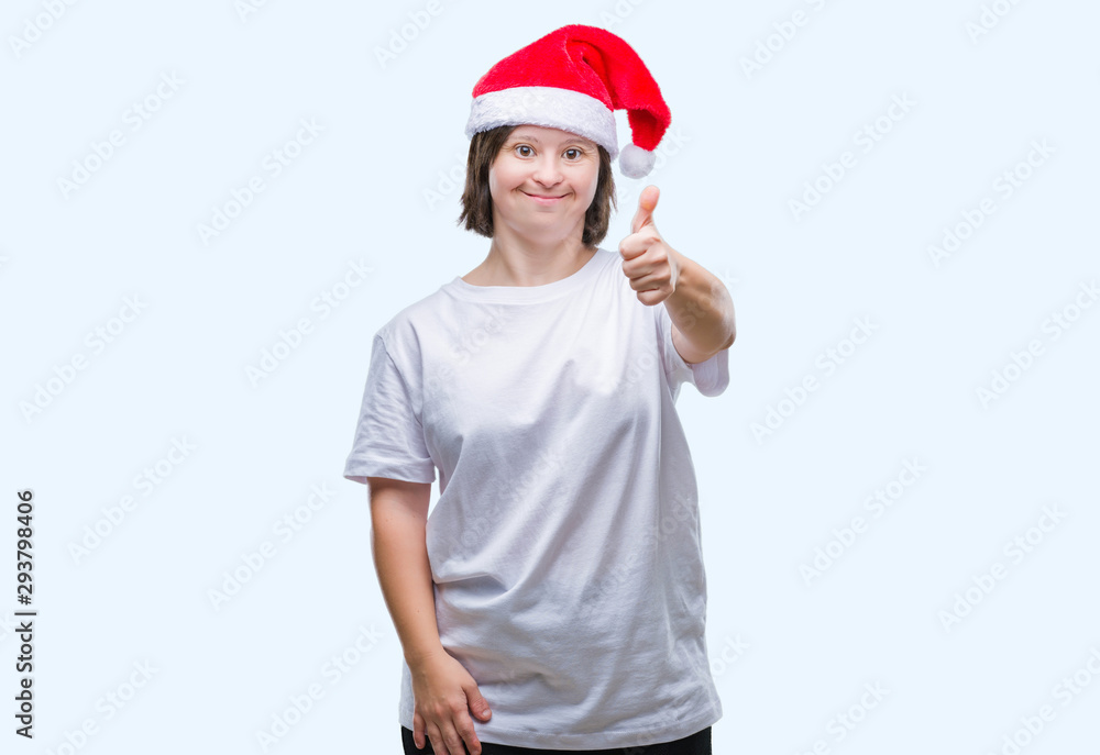 Young adult woman with down syndrome wearing christmas hat over isolated background doing happy thumbs up gesture with hand. Approving expression looking at the camera with showing success. Young adult woman with down syndrome wearing christmas hat over isolated background doing happy thumbs up gesture with hand. Approving expression looking at the camera with showing success.