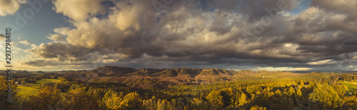 Autumn landscape at sunset - mountains, forests and beautiful clouds illuminated by the setting sun, hills of Bohemian Switzerland and Saxon Switzerland National Park, Czech Republic and Germany