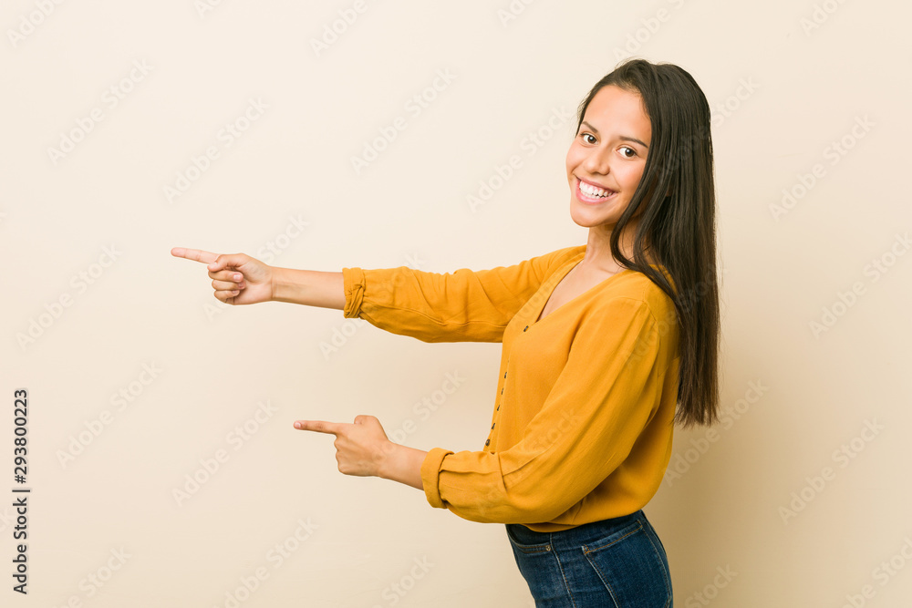 Young hispanic woman against a beige background excited pointing with forefingers away. Young hispanic woman against a beige background excited pointing with forefingers away.