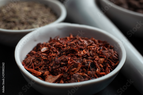 Spice red paprika in a white ceramic bowl next to a pounder on a black background