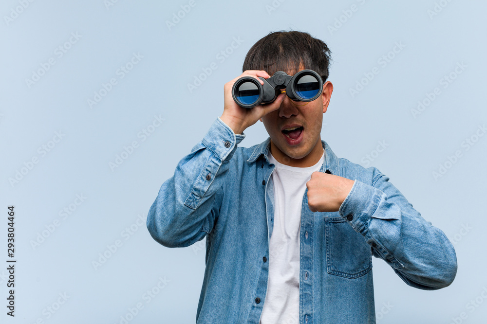 Young chinese man holding a binoculars surprised, feels successful and prosperous Young chinese man holding a binoculars surprised, feels successful and prosperous