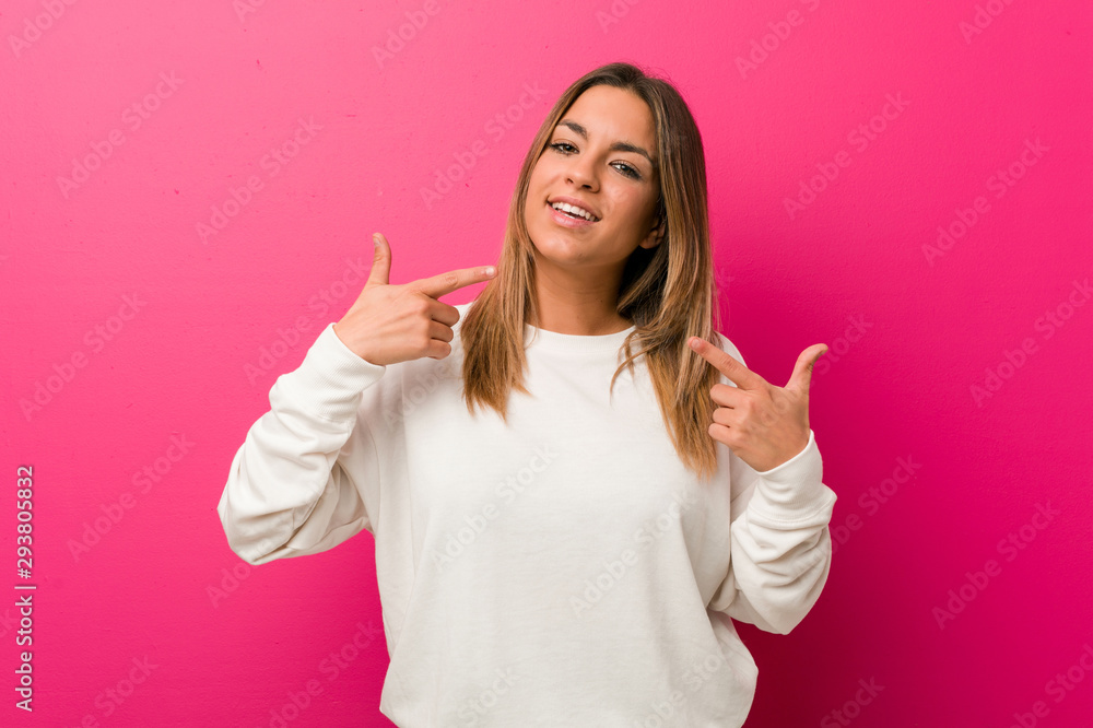 Young authentic charismatic real people woman against a wall smiles, pointing fingers at mouth. Young authentic charismatic real people woman against a wall smiles, pointing fingers at mouth.