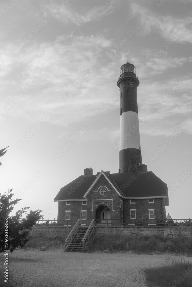 Black and white retro photo of old fashioned historic light house during day time used for maritime navigation on coast line shore