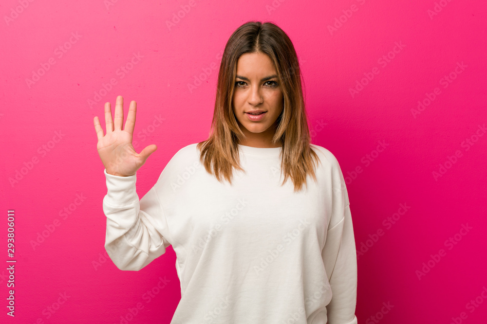 Young authentic charismatic real people woman against a wall smiling cheerful showing number five with fingers. Young authentic charismatic real people woman against a wall smiling cheerful showing number five with fingers.
