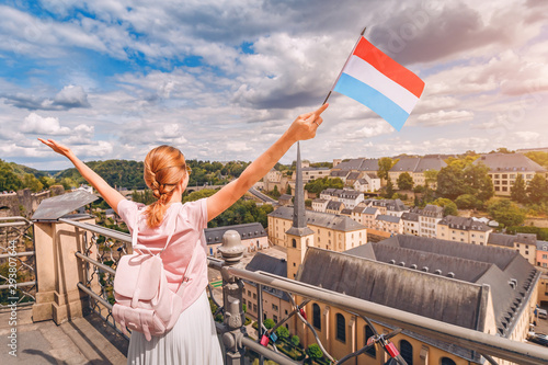 A happy traveller girl holds the flag of Luxembourg and admires the Grund area from the observation deck. Tourism, recreation and life in the country. photo