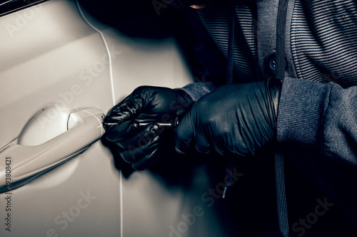 A man with a Balaclava on his head tried to break into the car. He uses a screwdriver. Hijacker, the concept of car theft.