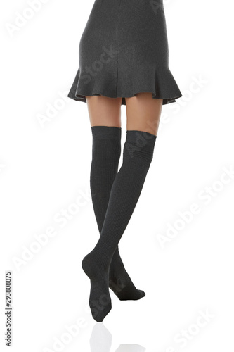 Medium back bottom shot of a female figure in the gray bell-shaped skirt and dark gray shadow-proof ribby stockings with closely rim on the top. The girl on tiptoe is posing on the white background.  photo