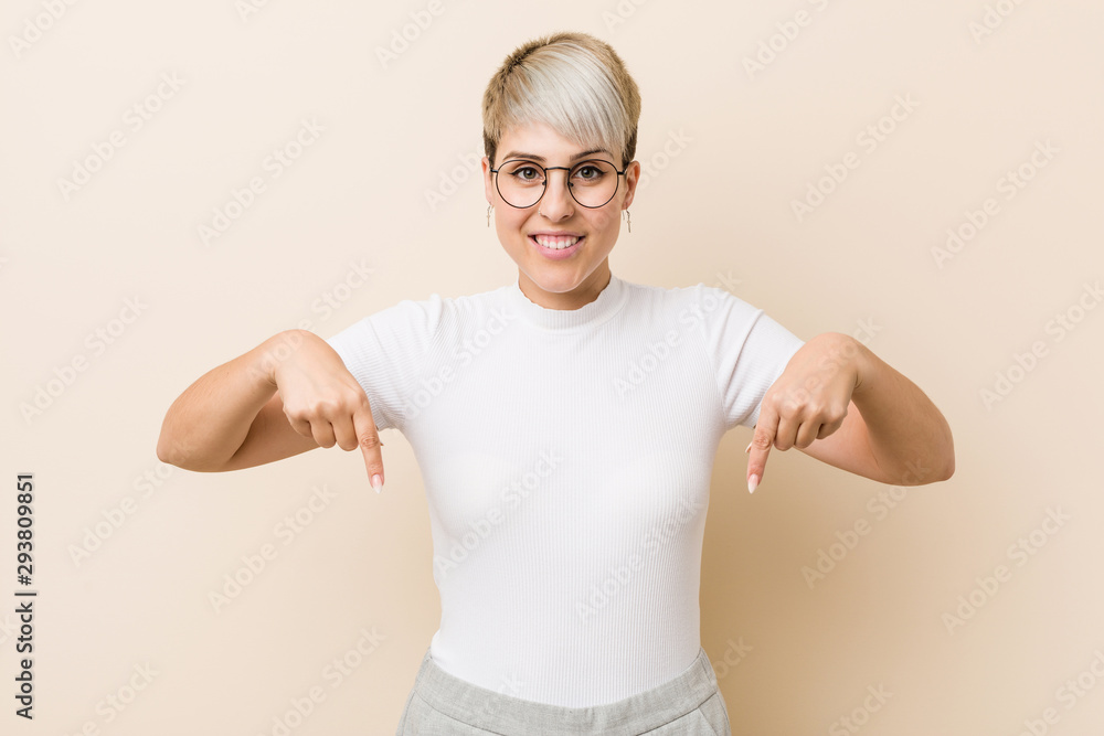 Young authentic natural woman wearing a white shirt points down with fingers, positive feeling. Young authentic natural woman wearing a white shirt points down with fingers, positive feeling.