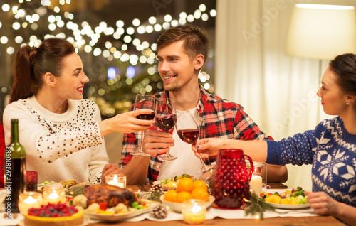 holidays and celebration concept - happy friends having christmas dinner at home  drinking red wine and clinking glasses