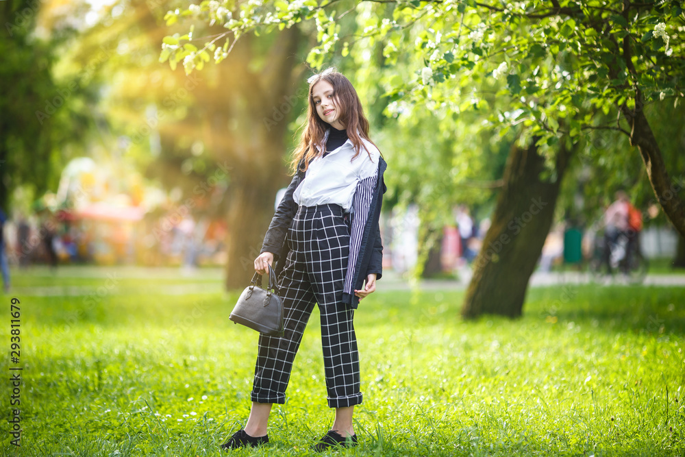 portrait of little beautiful stylish kid girl in city park on green forest background