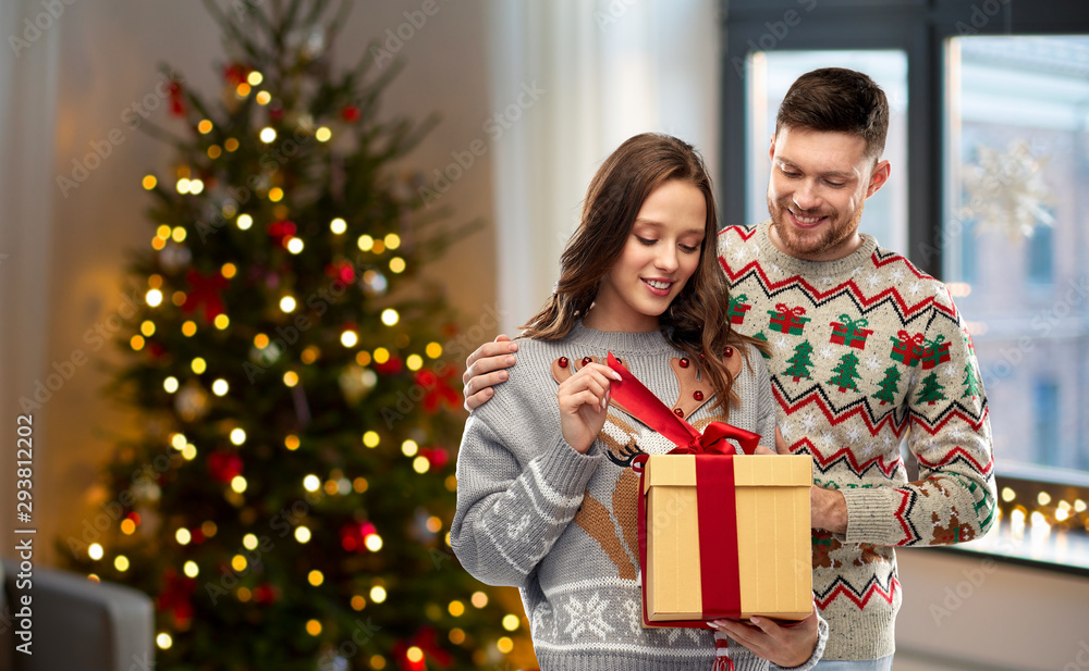 people and holidays concept - portrait of happy couple with christmas gift at ugly sweater party over home room background people and holidays concept - portrait of happy couple with christmas gift at ugly sweater party over home room background