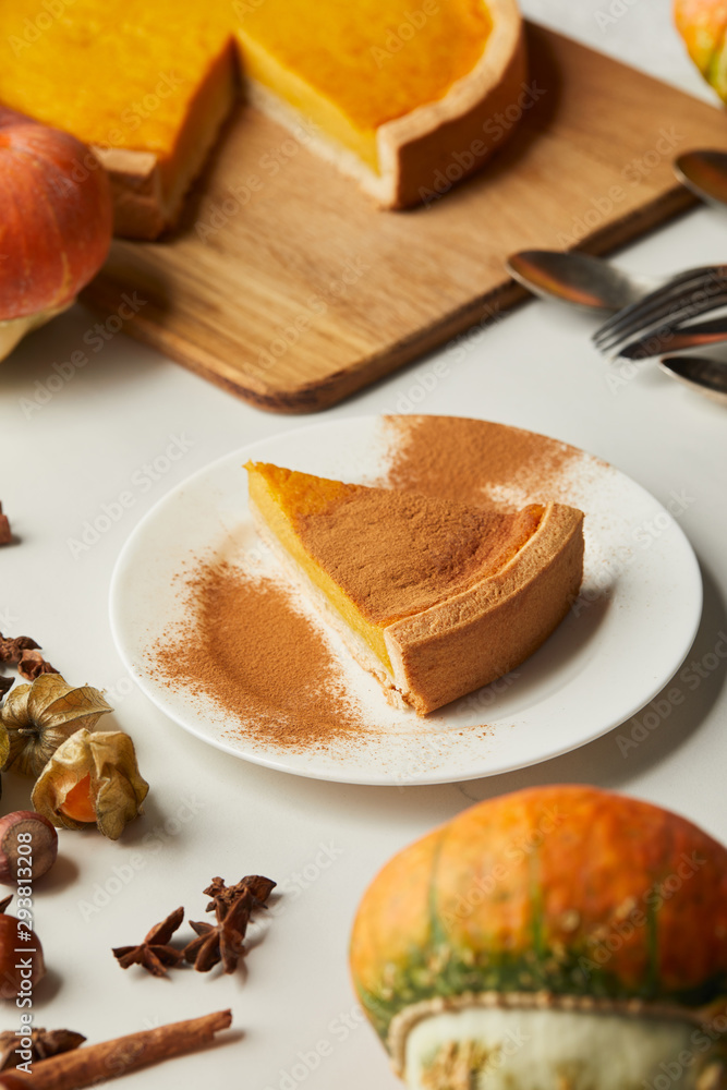 selective focus of tasty pumpkin pie near whole pumpkin and spices on white surface