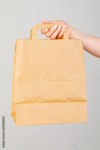Close-up of woman holding brown empty paper bag isolated on white background. The concept of service delivery