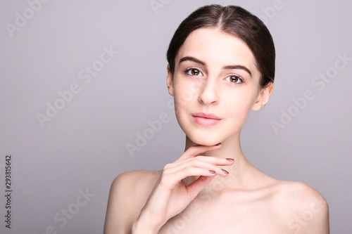 Portrait of young beautiful woman with perfectly clean face skin. Female with long black hair tied in ponytail smiling wide showing skincare results. Close up  copy space background.