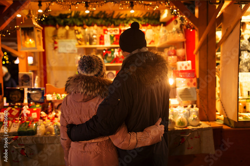 love, winter holidays and people concept - happy senior couple hugging at christmas market souvenir shop stall in evening