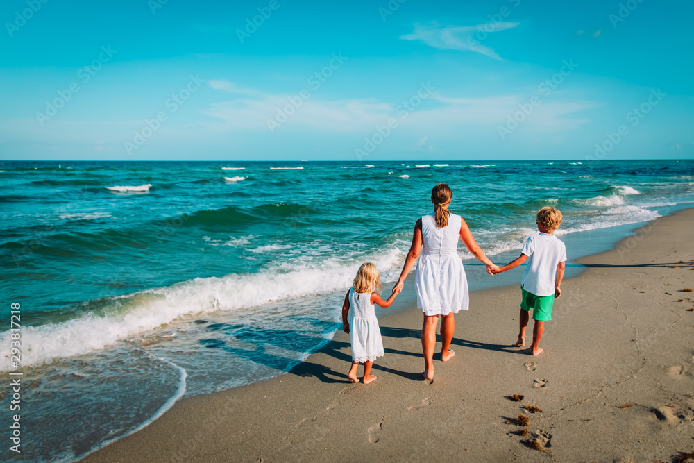 mother with son and daughter walking on beach at sunset