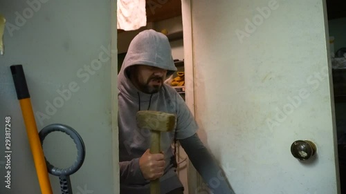 Wallpaper Mural A man in a sweatshirt holds a sledgehammer in his hand. Evil look. Bad intentions. Enters the door. The interior of the garage. Close-up. Torontodigital.ca