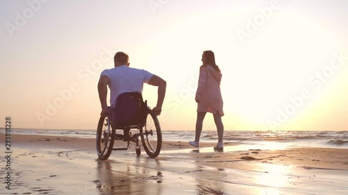 Handicapped man in wheelchair and his girlfriend on a beach at sunset