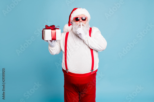 Hush its secret. Portrait of focused funny funky fat santa claus with big abdomen belly prepare gift for eve noel hold small giftbox wear red pants suspenders isolated over blue color background