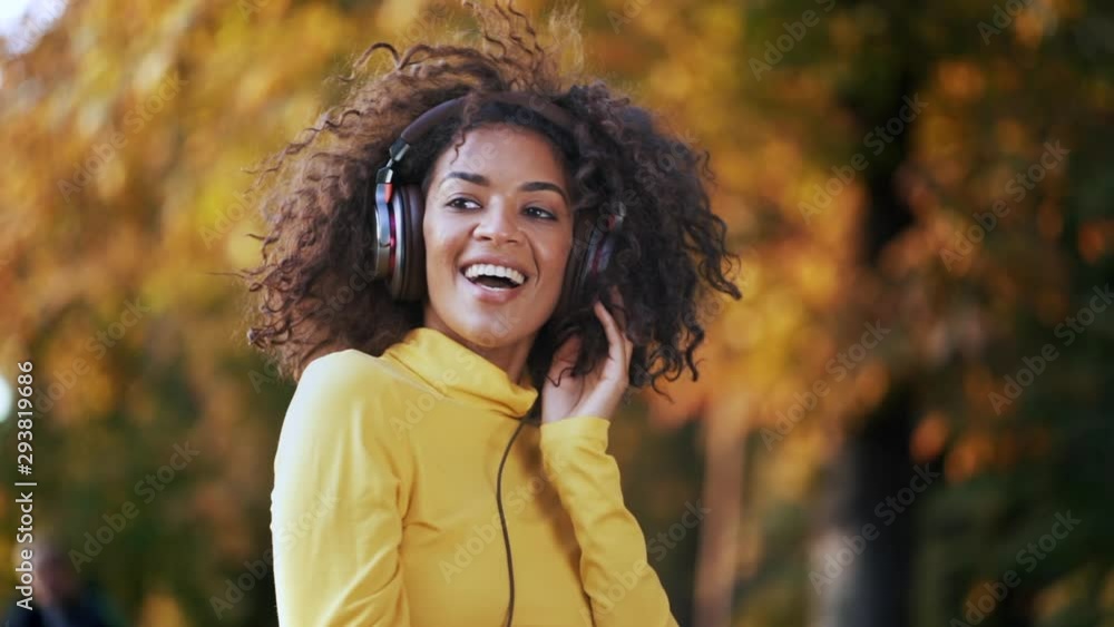 Close-up of african american girl's head dancing in white earphones. Young woman with curly hairstyle in yellow enjoys music in park. Slow motion Close-up of african american girl's head dancing in white earphones. Young woman with curly hairstyle in yellow enjoys music in park. Slow motion