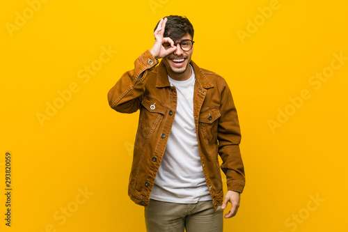 Young hispanic casual man excited keeping ok gesture on eye.