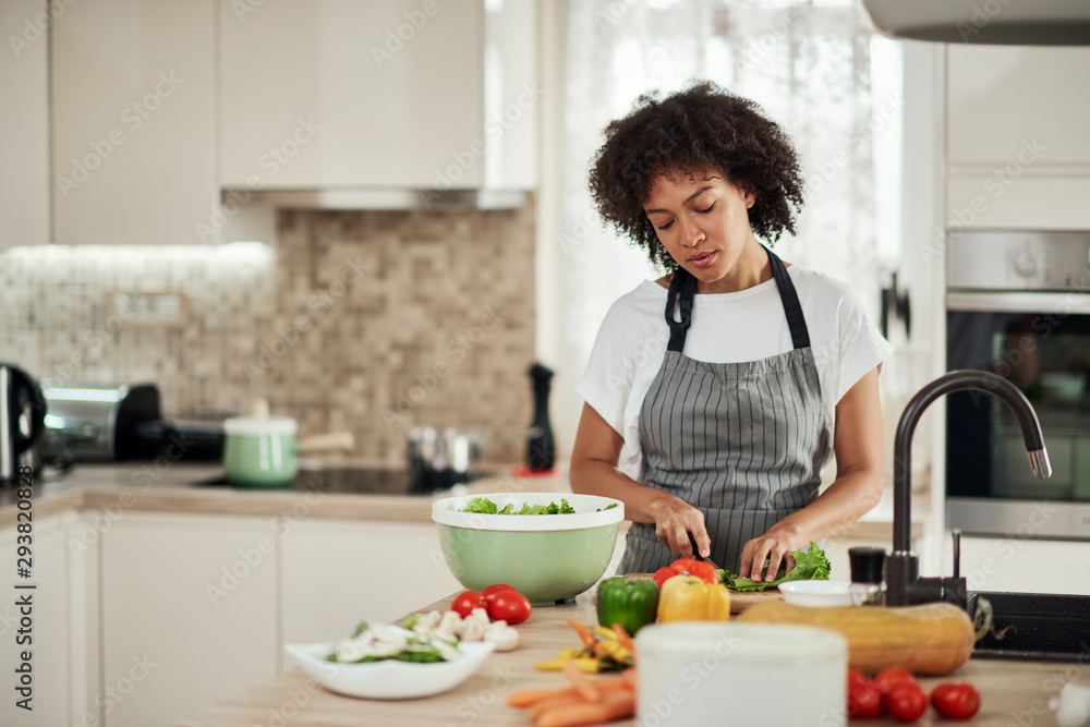 Attractive mixed race woman in apron cutting lettuce for salad. Kitchen interior. Attractive mixed race woman in apron cutting lettuce for salad. Kitchen interior.