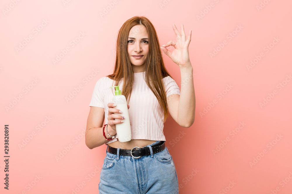 Young caucasian woman holding a cream bottle cheerful and confident showing ok gesture. Young caucasian woman holding a cream bottle cheerful and confident showing ok gesture.