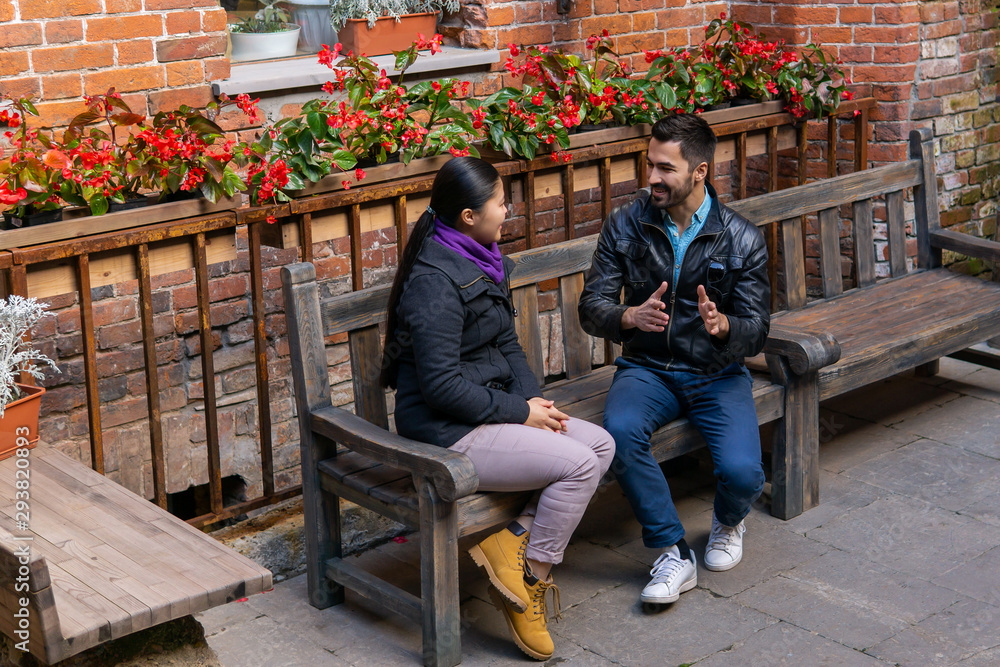young man and woman are having fun discussing something while sitting on a bench outdoors