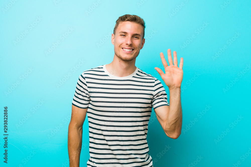 Naklejka premium Young caucasian man against a blue wall smiling cheerful showing number five with fingers.