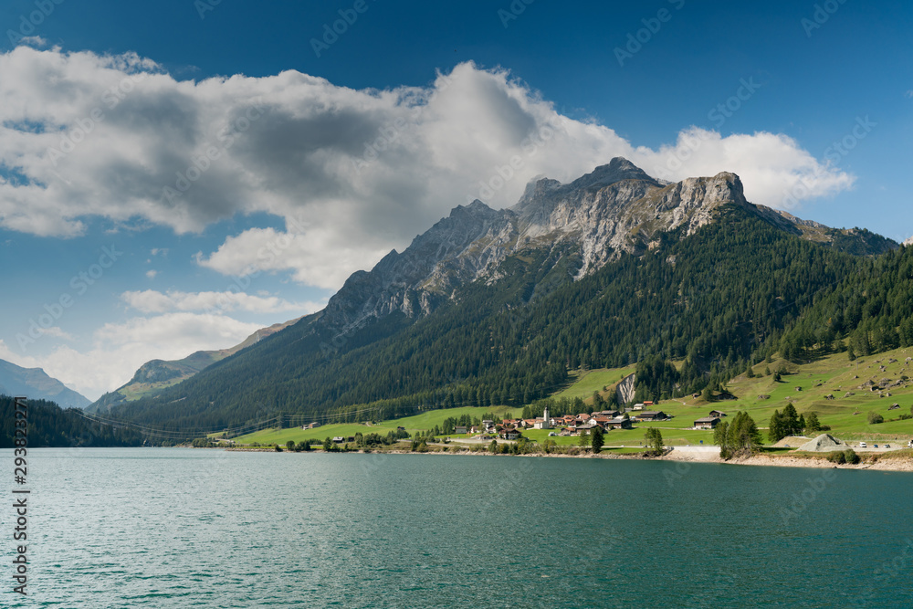 view of an idyllic and picturesque turquoise mountain lake surrounded by green forest and mountain peaks in the Swiss Alps